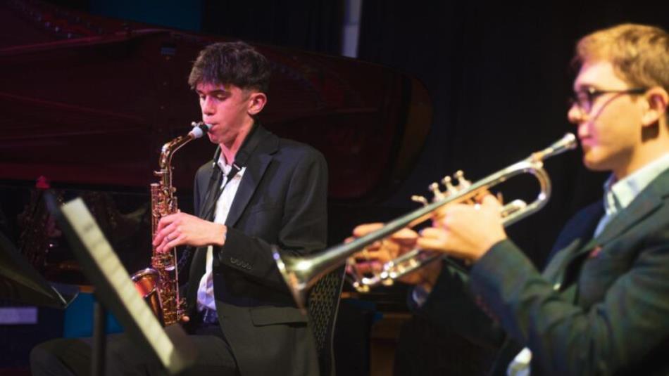 Two people sat down on stage playing brass instruments.