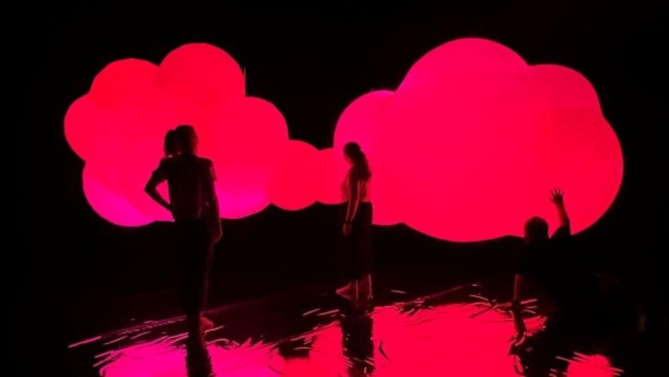 A light installation in a dark room of a red cloud and people interacting with it.