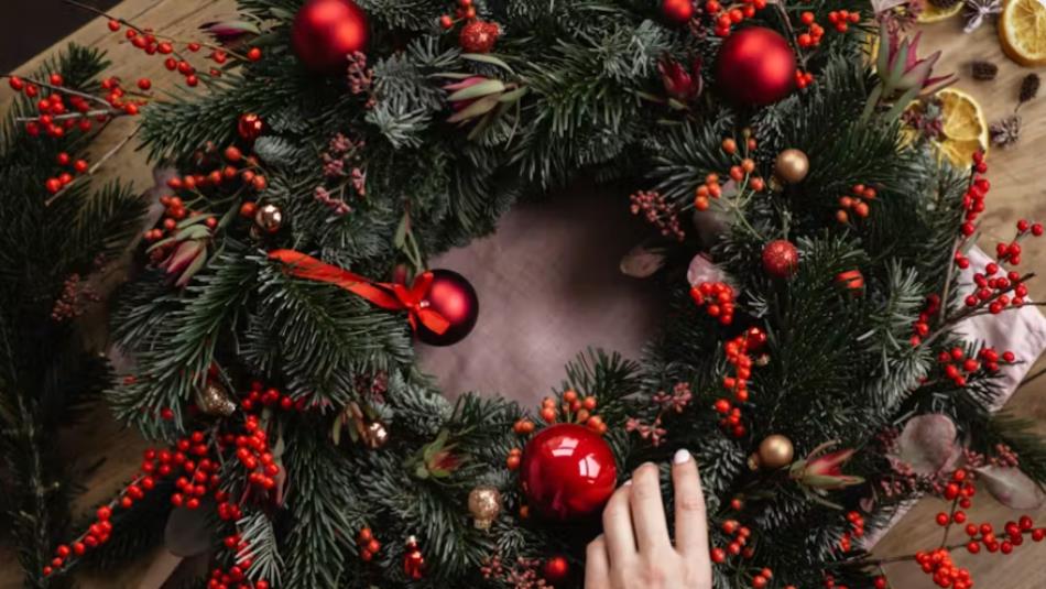 A person tending to a festive wreath decorated with red baubles on a table.