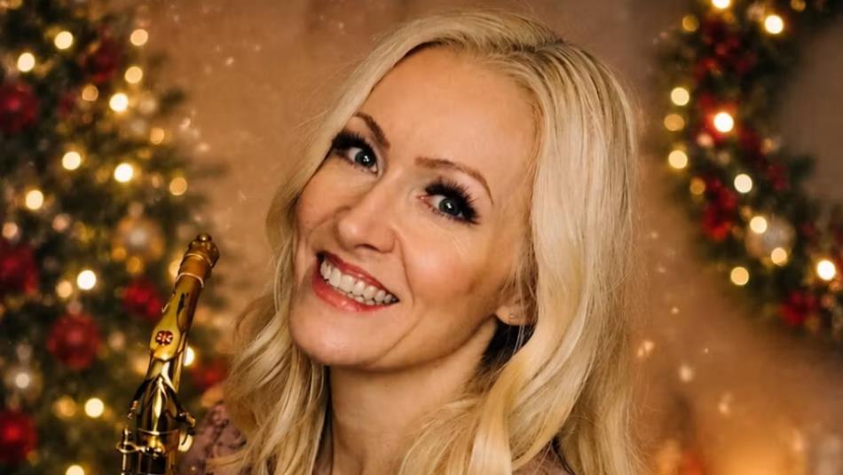 A person smiling holding a saxophone with a festive wreath and a sparkling Christmas tree in the background.