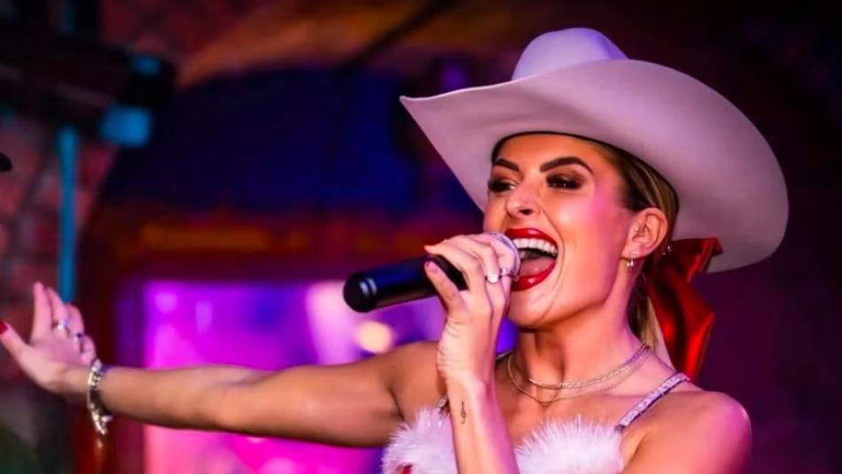 A person singing wearing a cowboy hat and a red ribbon.