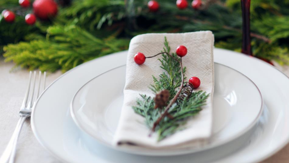 A festive table spread, with pine needles and red berries decorating the plates.