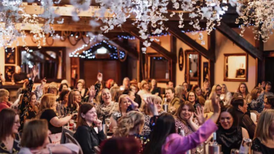 People in a festive hall playing bingo with their arms raised in the air.