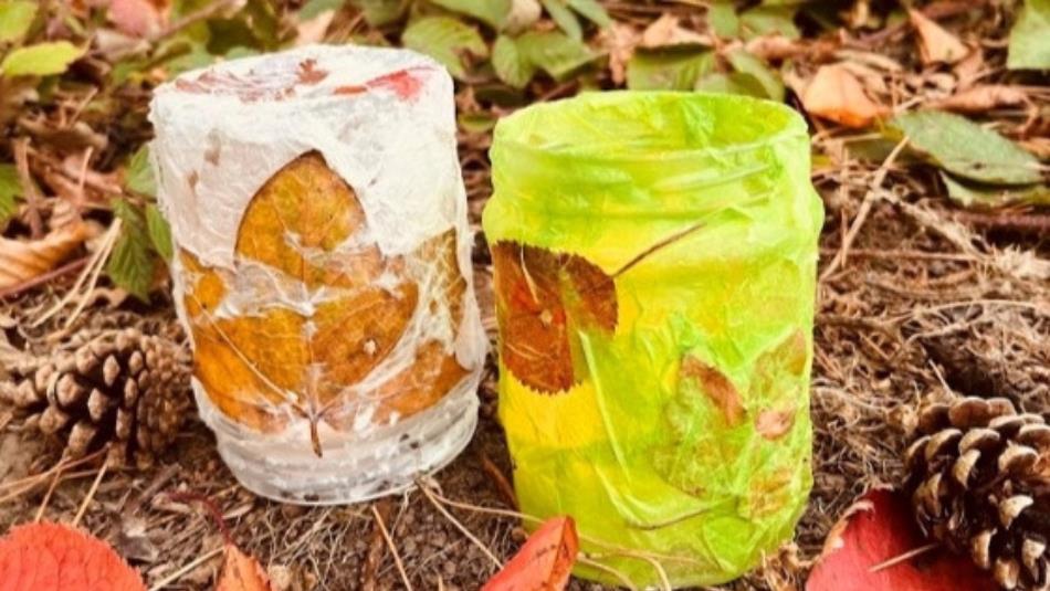 Two glass jars decorated with leaves, surrounded by autumnal foliage.