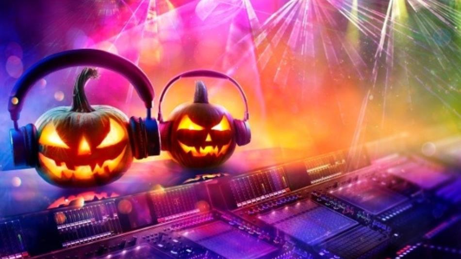 A DJ deck with two carved pumpkins wearing headphones on top, under colourful lighting.