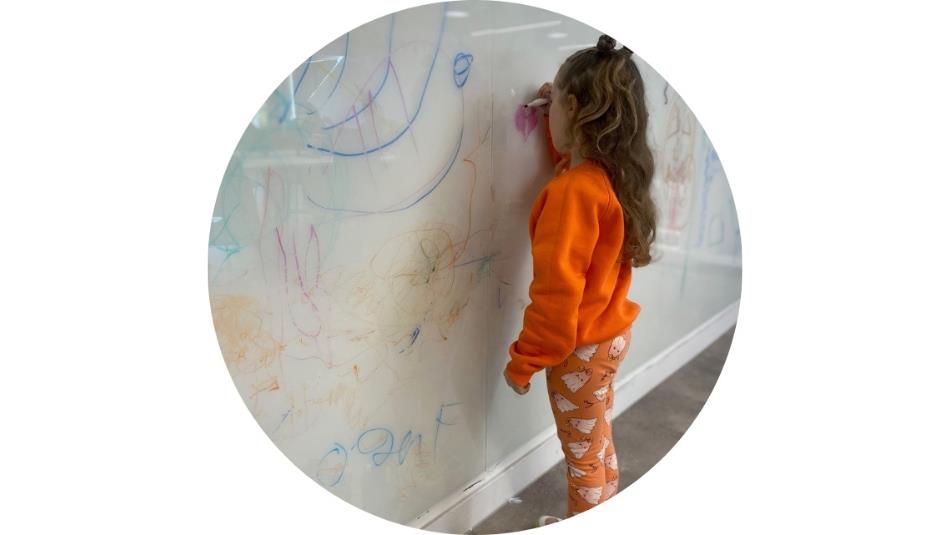 A small child wearing orange, drawing on a wall.