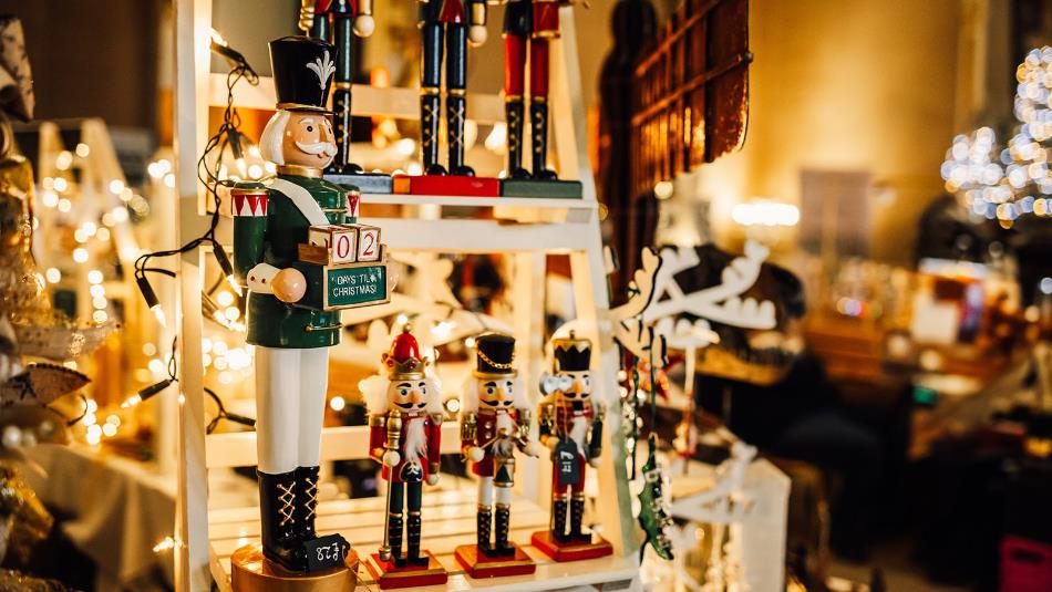 A selection of festive nut cracker soldiers lined up on a Christmas market stall surrounded by warm fairy lights.