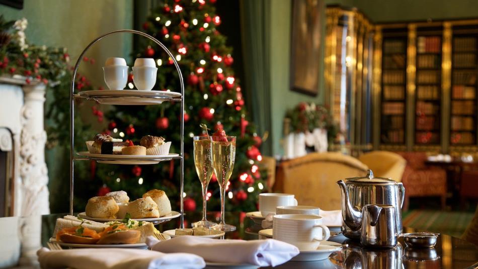 A festive afternoon tea spread, with a selection of pastries, tea and champagne with a Christmas tree in the background.
