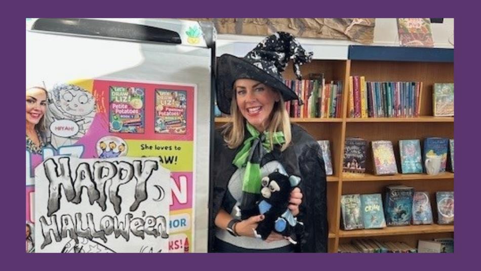 A person, smiling dressed as a witch holding a toy cat in a library. On a purple background.