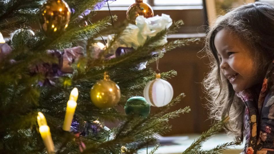 A small child smiling at a decorated Christmas tree.