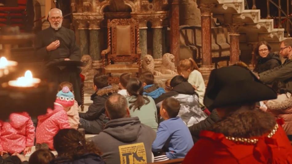 A group of children and adults sat in a church setting listening to a speaker.