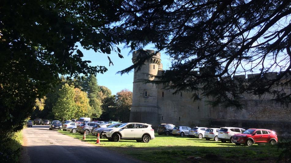 A landscape view of a turret of Brancepeth Castle, through the silhouette of trees and a carpark.