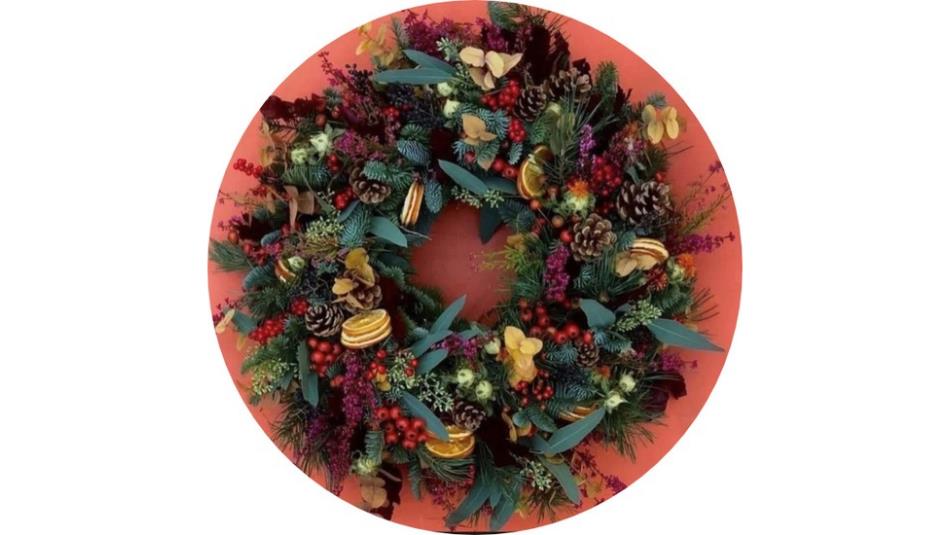A festive wreath decorated with dried oranges and pine cones on a light pink table in a circle on a white background.