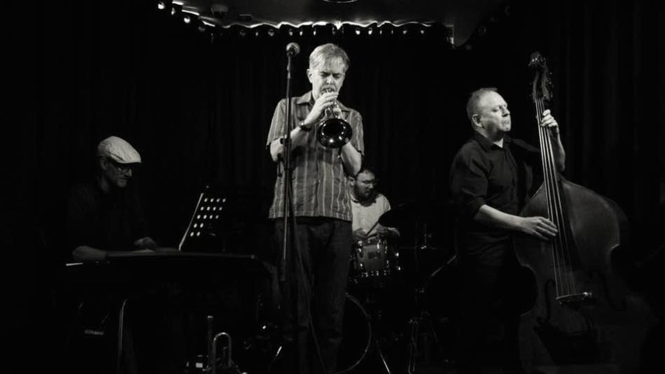 Jazz musicians on a dark atmospheric stage, in black and white.