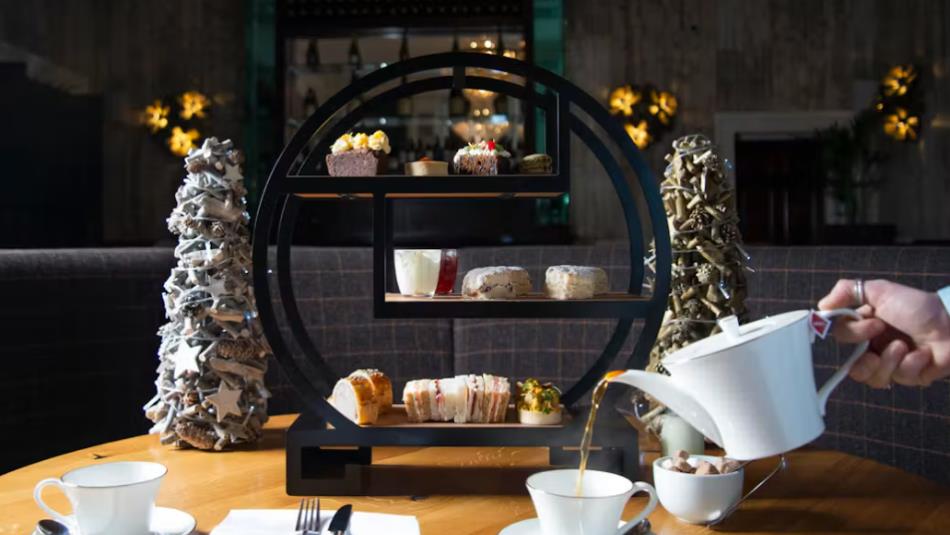 A festive afternoon tea spread, with small christmas trees, and a person pouring a cup of tea.