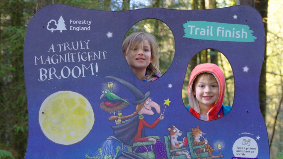 Two children poking their heads through a Room On A Broom themed pop up stand, in Hamsterley Forest.