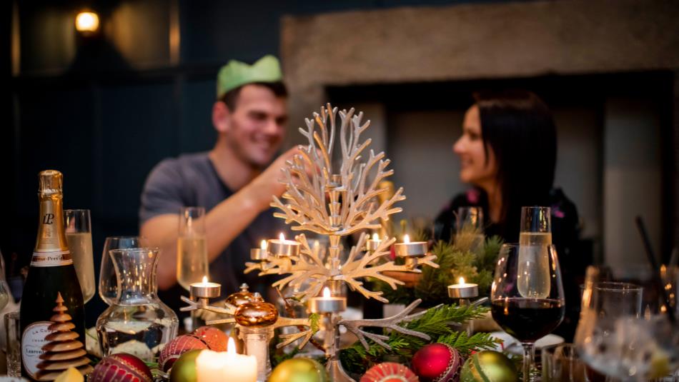 A couple enjoying a festive meal in paper crowns, surrounded by food and candles