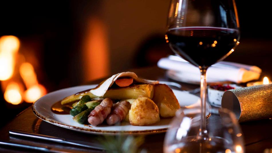 Close up of a festive meal, pigs in blankets, roast potatoes and parsnips, with a glass of red wine at the side