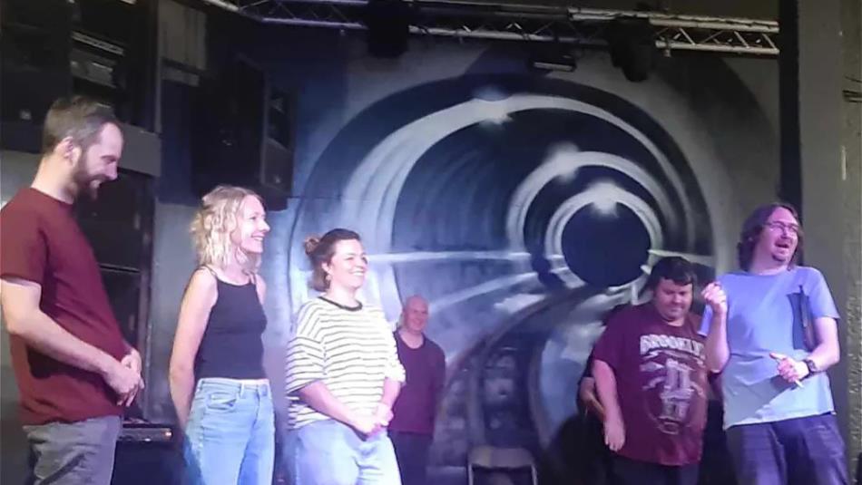 A group of people standing on stage and smiling, bright lights shine down on them