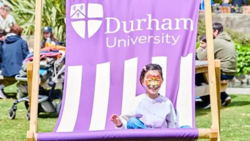 Small child, with face paint, sat on a large Durham University themed, purple deck chair in the Botanic Garden