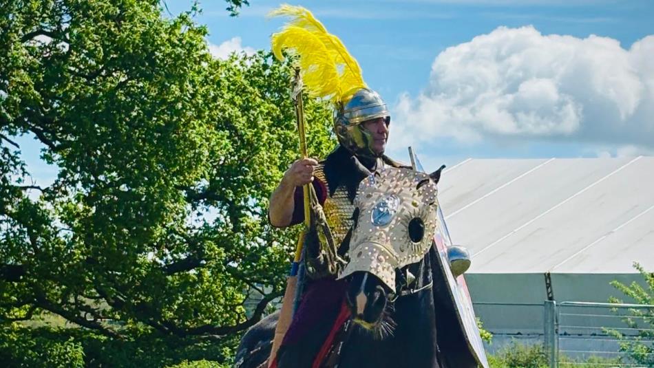 Roman actor sat on top of a horse with roman armour and a shield.