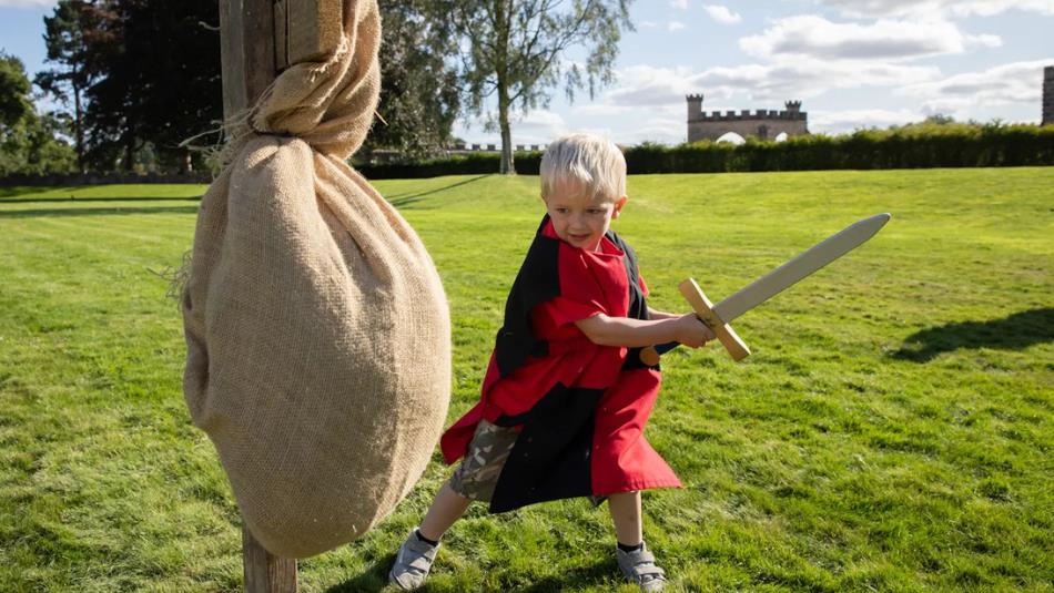 Small child dressed as a knight, hitting a training post with a wooden sword at Auckland Palace