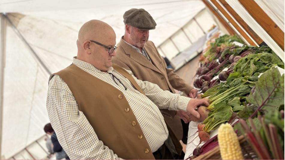 Two people wearing vintage style clothing inspecting rows of vegetables in a tent at Beamish.
