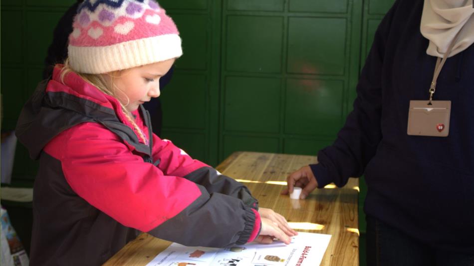 Small child in a hat, working on a worksheet on a table in Beamish