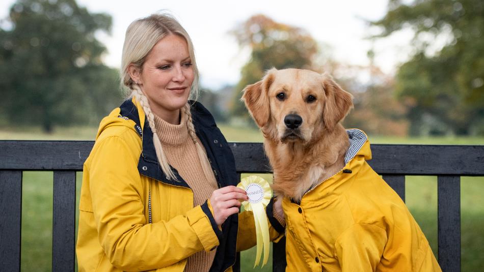 Bark in the Park Dog Show - Woman and her dog in matching yellow coats, sitting on a bench.