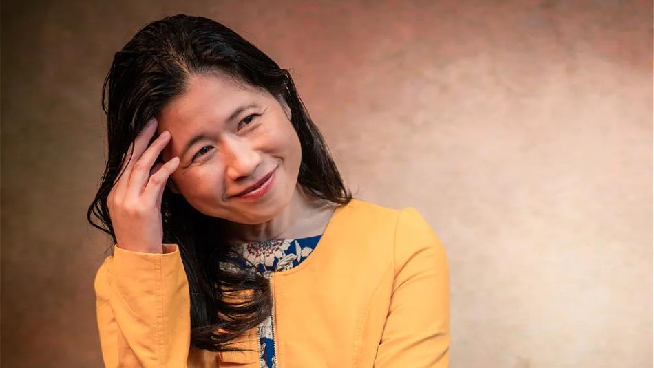 Person wearing a yellow jacket, smiling off to the side, holding their head .