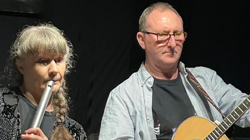 Couple playing the guitar and flute against a black background