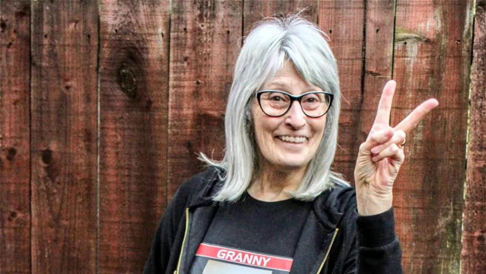 Person wearing glasses doing a peace sign in front of a wooden fence