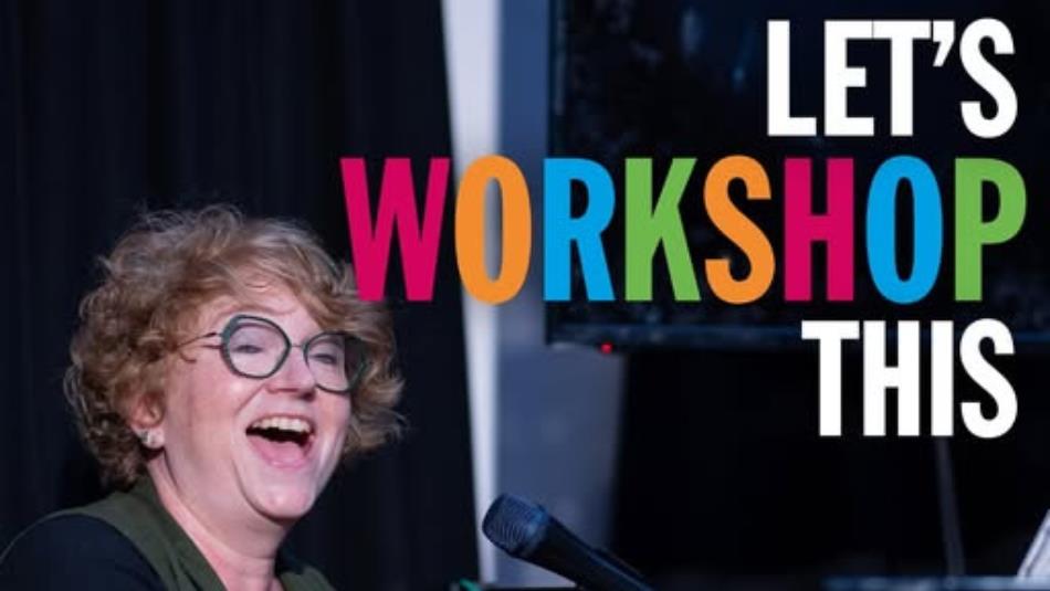 Person wearing glasses, smiling with their mouth open sat at a piano with a microphone.