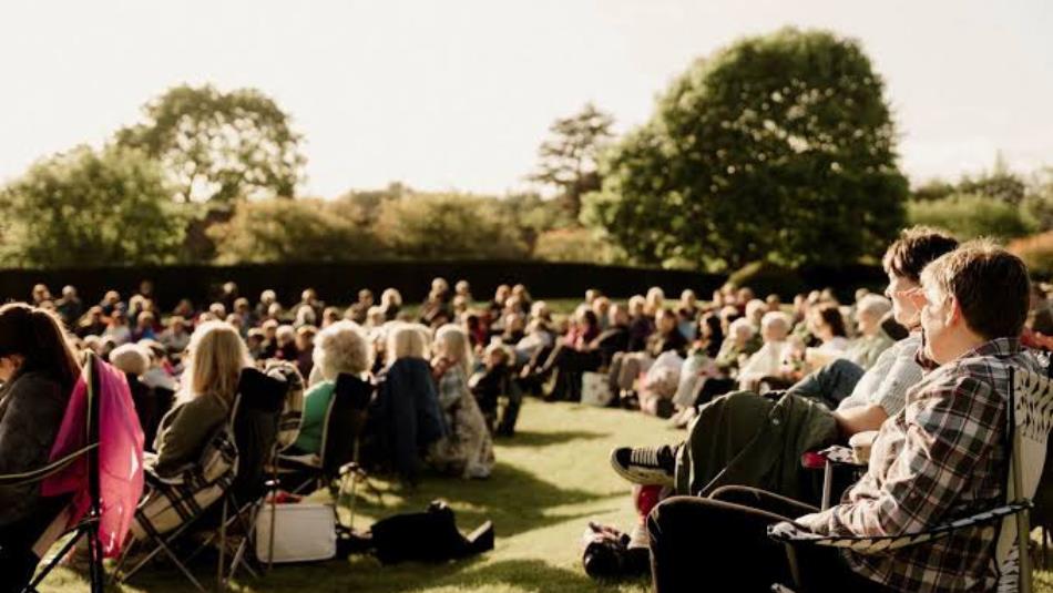 Group of people sat on garden chairs, at Raby gardens in the sun