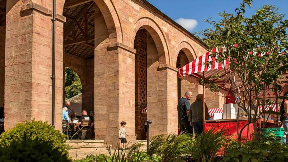 Landscape view of an archway building at Raby Castle, with a striped market stall outside in the sun