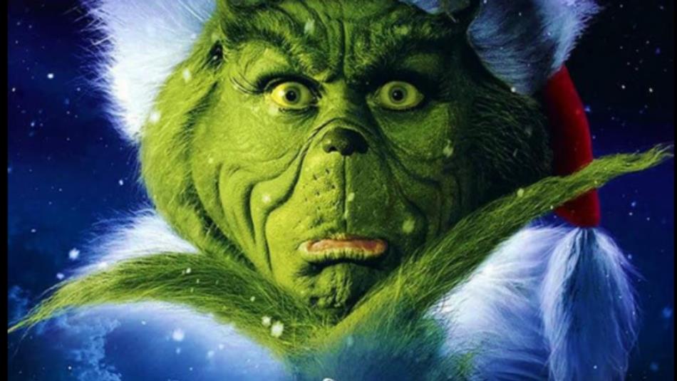 Close up of the Grinch looing quizzical at the camera wearing a Santa hat in the snowy night