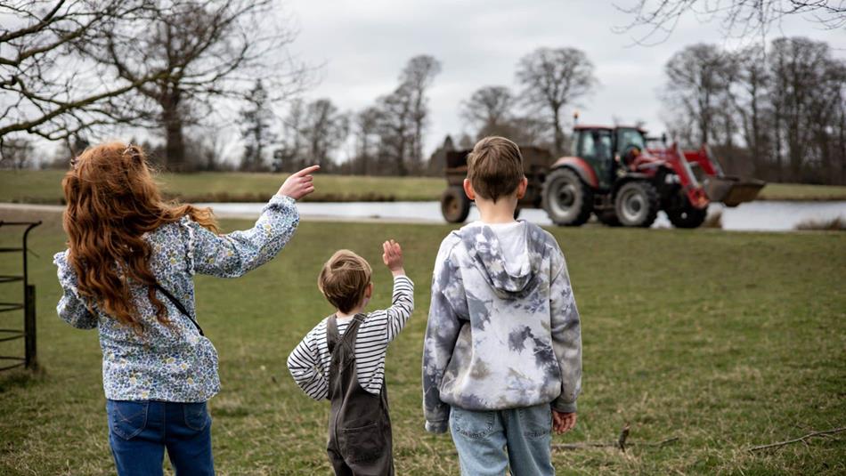 Three children pointing at a tractor in front of the lake at Raby Castle.
