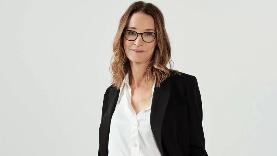 Susie Dent in a black blazer against a grey background.