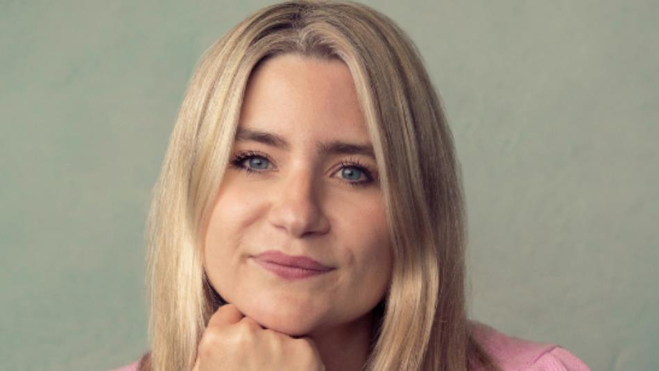 Harriet Kemsley with her chin resting on her hand, smiling with a beige background.