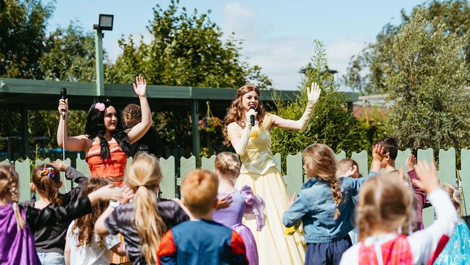 Two women dressed as princesses with a crowd of children dancing