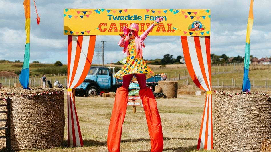 Woman on stilts in front of Tweddle Farm Carnival banner