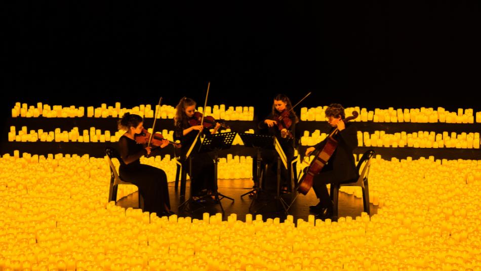 Group of musicians playing string instruments surrounded by hundreds of candles.