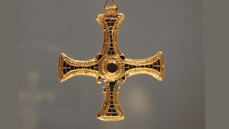 A gold cross pendant with arms inlaid with precious stones.