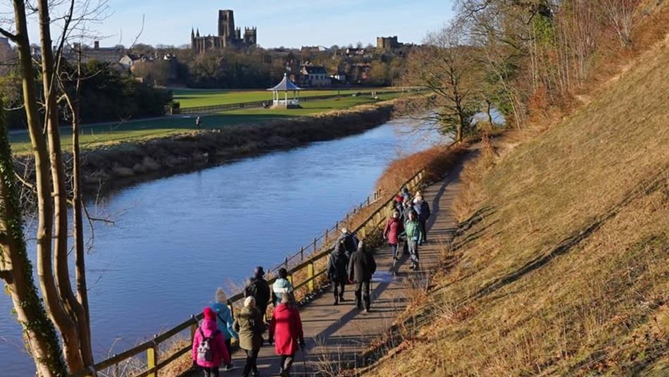 A group walking along the River Wear, with stunning views of the bandstand and Durham Cathedral and Castle.