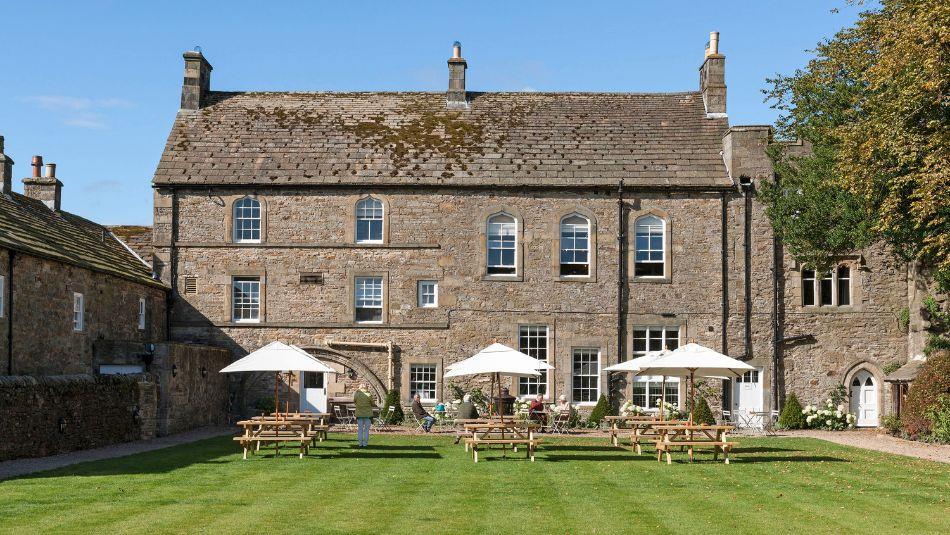 View of the Lord Crewe Arms on a bright sunny day with people sat in the garden under white umbrellas.