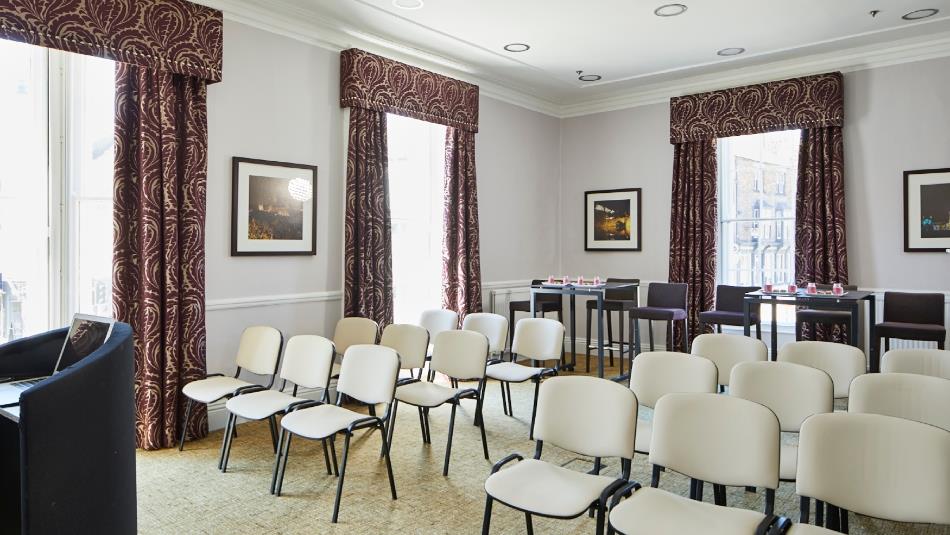 Neville room set up theatre style with white chairs
Light coloured walls with dark red, patterned curtains on 3 windows