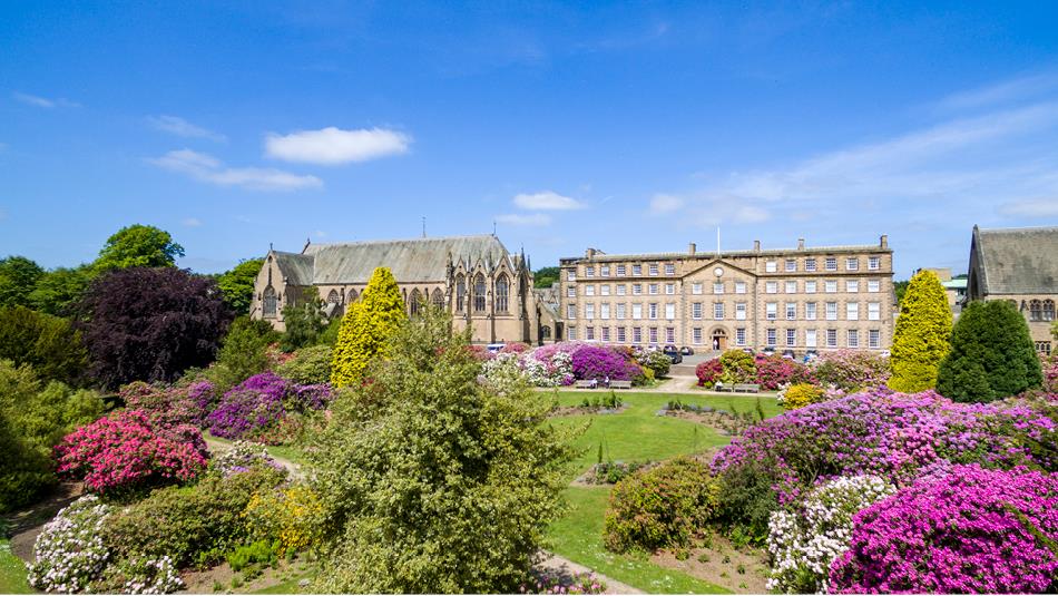 Ushaw and grounds on a bright, clear day, surrounded by purple shrubs.