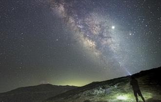 Silhouette of a person photographing The Milky Way from the hillside