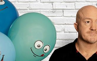 Image of Andy Parsons next to balloons with smiling faces.