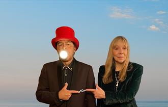 Charlie Dore and Julian Littman standing side by side with their fingers pointing towards each other and electricity flowing between them.